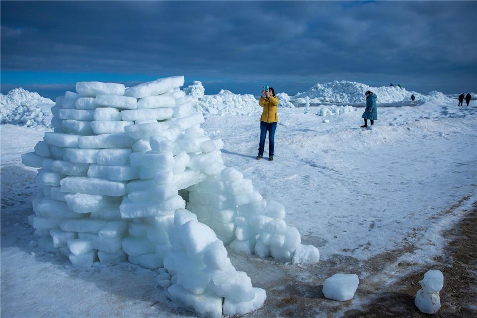 Eine Frau fotografiert ein aus Eisstücken gebautes Iglu vor meterhohen Eisbergen am Ostseestrand auf der Insel Usedom. Jens Büttner/dpa