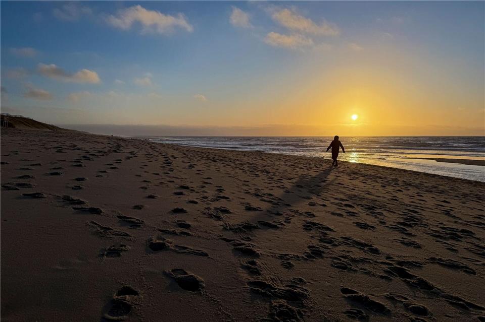 Eine Frau geht im Licht der tief stehenden Sonne am Strand bei Rantum auf Sylt spazieren.Christian Charisius/dpa