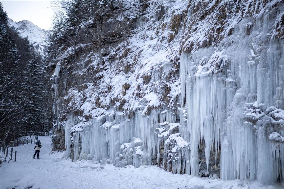 Eine Frau geht mit ihrem Kind auf einem Weg an Eiszapfen vorbei. Gian Ehrenzeller/KEYSTONE/dpa