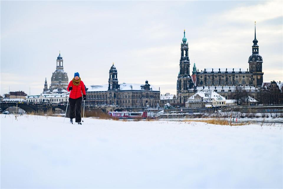 Eine Frau läuft am verschneiten Elbufer vor der historischen Altstadtkulisse in Dresden SkiRobert Michael/dpa