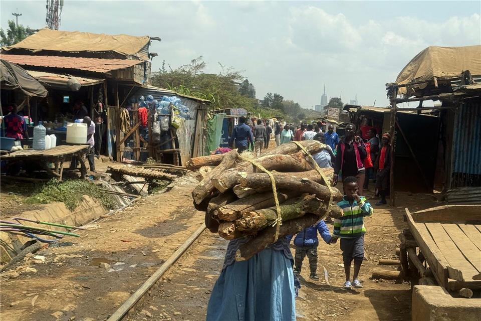 Eine Frau trägt ein Bündel Brennholz entlang der Bahnstrecke, die durch Nairobis größten Slum Kibera führt. (Archivbild)Eva Krafczyk/dpa