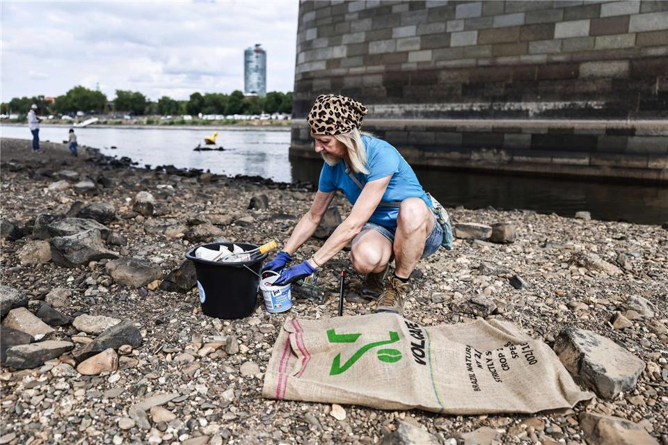 Eine Freiwillige der Initiative „Blockblocks“ sammelt bei Niedrigwasser Müll am Ufer des Rheins.Oliver Berg/dpa