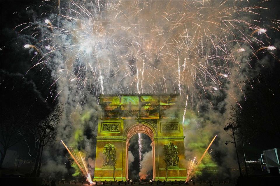 Eine Lichtshow wird auf den Arc de Triomphe projiziert, während ein Feuerwerk im Rahmen der Neujahrsfeierlichkeiten auf den Champs Elysees gezündet wird.Christophe Ena/AP/dpa