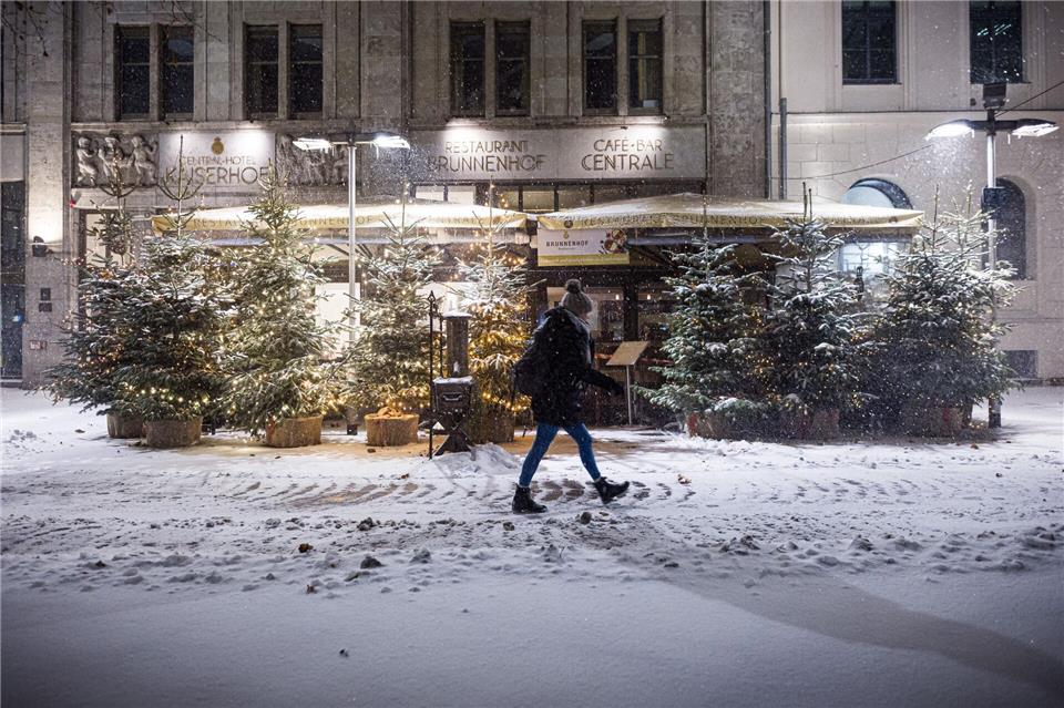 Eine Passantin geht am frühen Morgen im dichten Schneefall an Weihnachtsbäumen im Zentrum entlang.Moritz Frankenberg/dpa