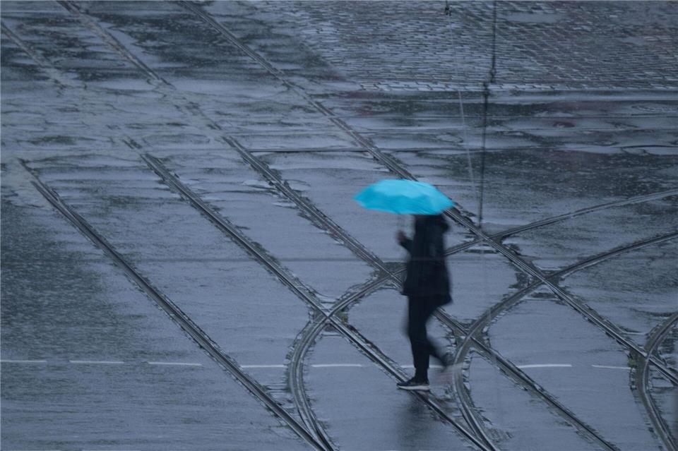 Eine Person geht bei Regen mit einem blauen Regenschirm über eine Straße in Dresden.Katharina Kausche/dpa