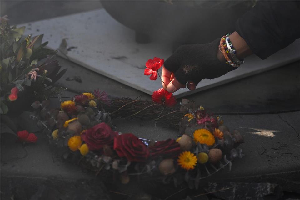 Eine Person legt eine Mohnblume an der Gedenkstätte „Für unser Land“ während der Gedenkfeier für Aborigines und Torres-Strait-Insulaner (ATSIVA) im Rahmen des Anzac-Tags am Australian War Memorial in Canberra nieder.Lukas Coch/AAP/dpa