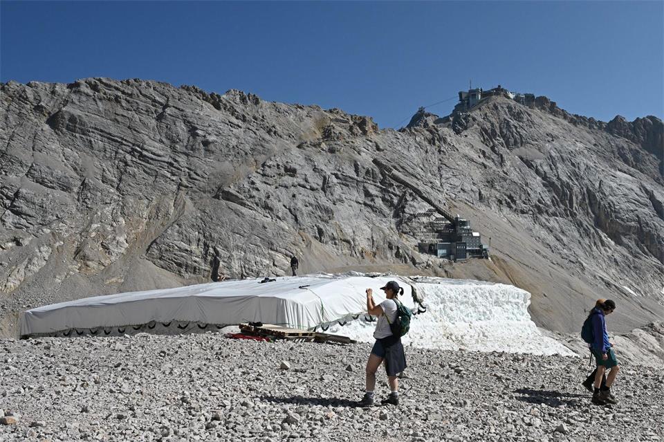 Eine Person macht Fotos neben Abdeckfolien auf einem Schneedepot neben den Überresten des Nördlichen Schneeferner-Gletschers auf der Zugspitze.Angelika Warmuth/dpa