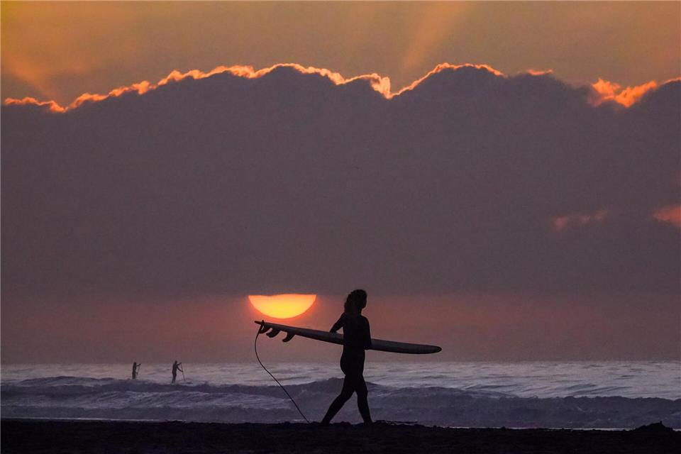 Eine Surferin trägt ihr Surfbrett in Richtung Meer.Richard Ellis/ZUMA Press Wire/dpa