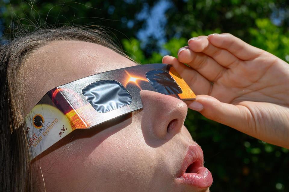 Eine junge Frau schaut durch eine Sonnenfinsternisbrille und betrachtet die Mittagssonne.Patrick Pleul/dpa