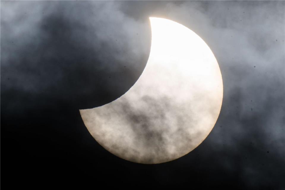 Eine partielle Sonnenfinsternis ist zwischen Wolken am Himmel zu sehen. (Archivbild)Julian Stratenschulte/dpa