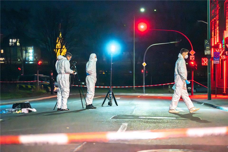 Einsatzkräfte sichern Spuren auf der Straße vor dem Tatort.Vincent Kempf/dpa