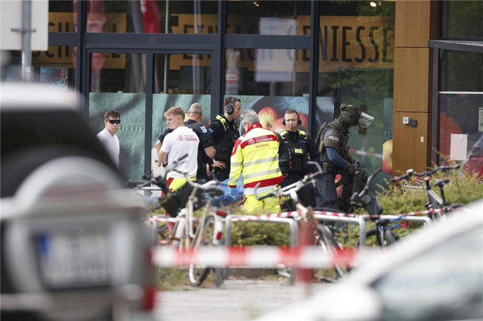 Einsatzkräfte stehen vor einem Supermarkt neben einer verletzten Person auf einer TrageCarsten Koall/dpa