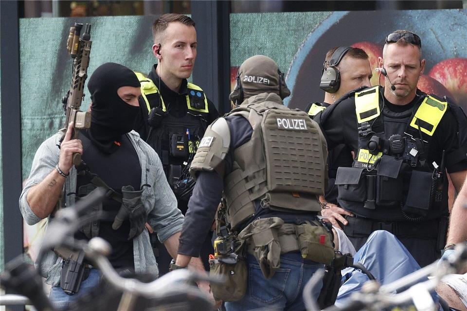 Einsatzkräfte stehen vor einem Supermarkt neben einer verletzten Person auf einer Trage.Carsten Koall/dpa