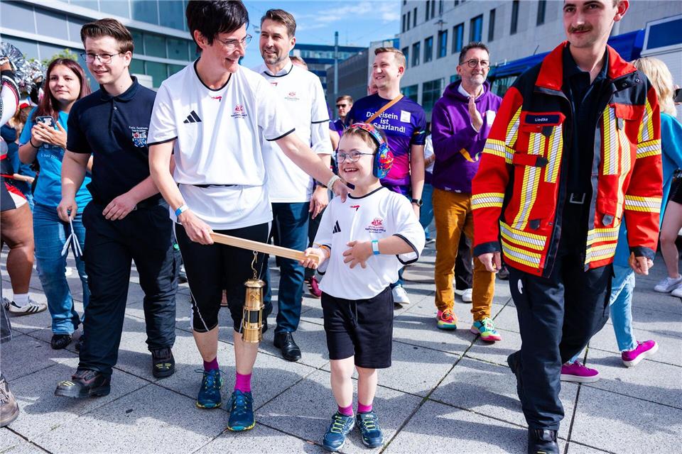 Elias (8) trägt gemeinsam mit seiner Mutter Stephanie Lade die Grubenlampe, das Symbol des Fackellaufs der Special Olympics, auf einem Holzträger durch die Saarbrücker Innenstadt.Laszlo Pinter/dpa