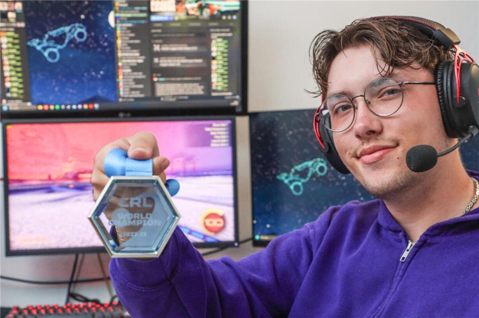 Fabian Buß sitzt in seinem Zimmer in Bocholt vor seinem Gaming-PC mit dem Spiel Rocket League. Er zeigt die WM-Medaille, die er 2023 in Dallas gewonnen hat.