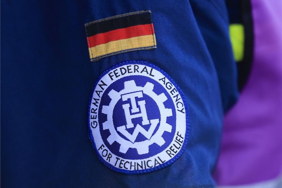 Fahne und Logo des Technischen Hilfswerk (THW) hängen an der Jacke eines Mitarbeiters.