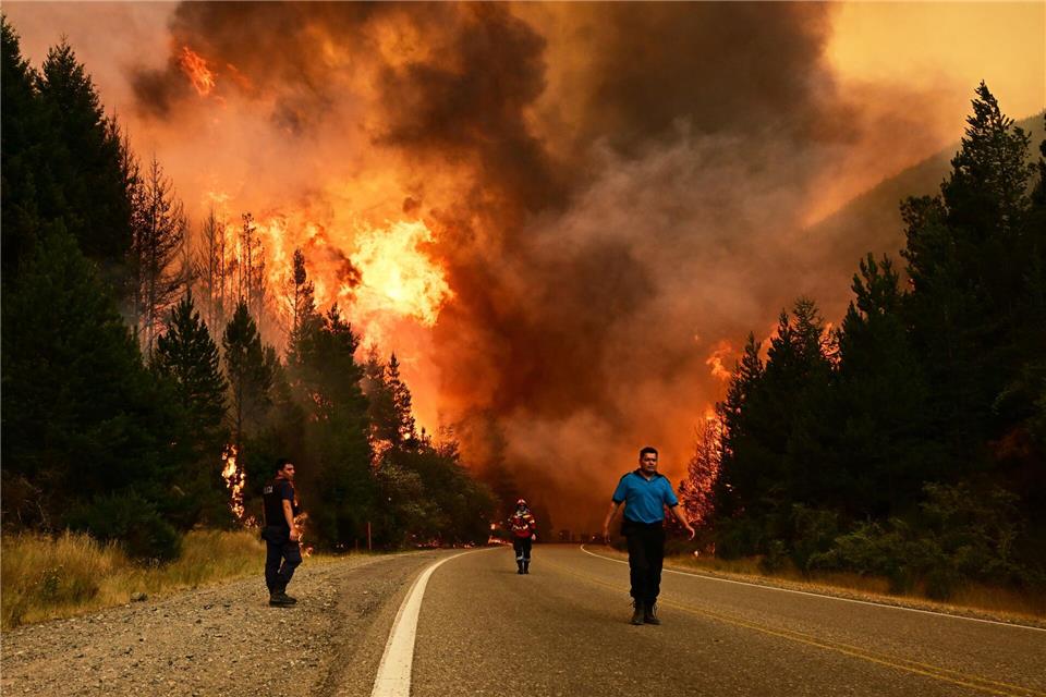 Feuerwehrleute gehen auf einer Straße während eines Waldbrandes in Argentinien.Maxi Jonas/AP/dpa