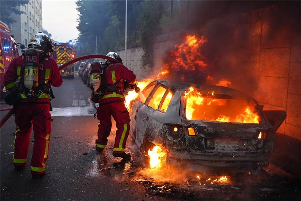 Frankreich: Regierung erlässt Beschränkungen nach Krawallen Feuerwehrleute löschen am Rande von Ausschreitungen westlich von Paris ein brennendes Auto.