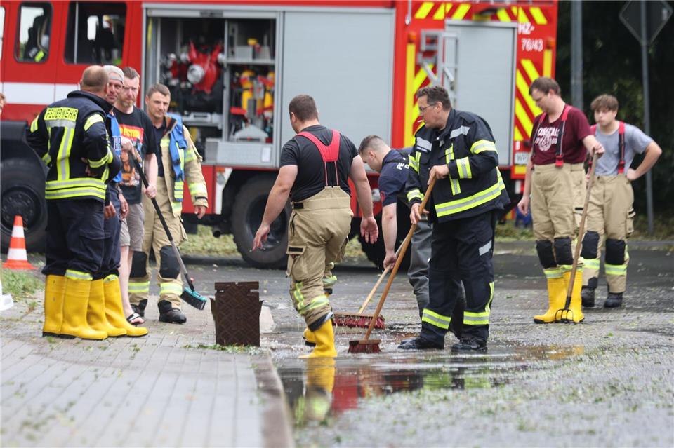 Feuerwehrleute reinigen nach Starkregen eine überflutete Straße in Derenburg.Matthias Bein/dpa