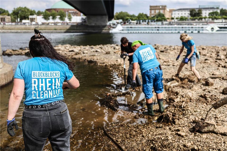 Freiwillige versuchen bei einer Müllsammelaktion bei Niedrigwasser am Rhein einen großen Reifen auszugraben. (Archivbild)Oliver Berg/dpa