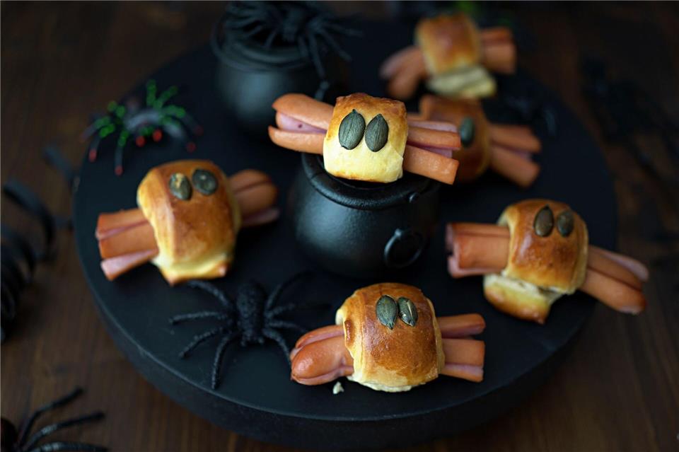 Für die Würstchenspinnen werden die an den Enden eingeschnittenen Wienerstückchen mit Teigstreifen umwickelt. Darauf drückt man je zwei Kürbiskerne als Augen und schiebt das Ganze in den Backofen.Mareike Pucka/biskuitwerkstatt.de/dpa-tmn