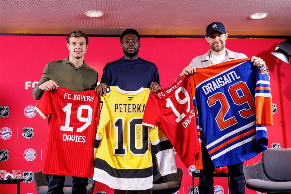 Fußball und Eishockey als Partner: Die deutschen Eishockeystars John-Jason Peterka (l) und Leon Draisaitl (r) mit dem kanadischen Bayern-Profi Alphonso Davies.  Matthias Balk/dpa