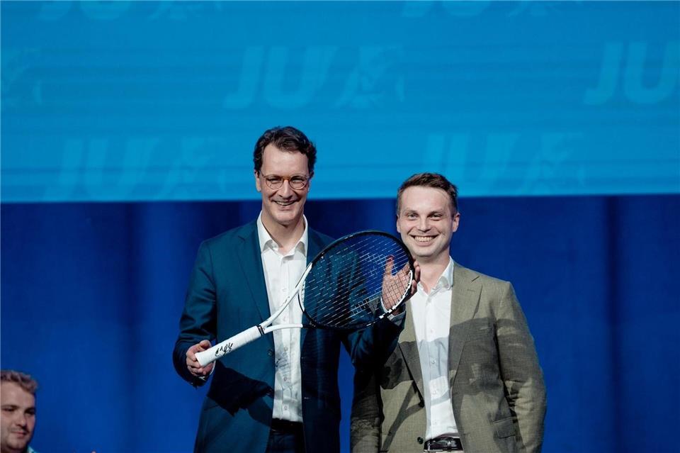 Hendrik Wüst (CDU, l), Ministerpräsident von Nordrhein-Westfalen, steht mit einem Tennisschläger auf der Bühne des NRW-Tags der Jungen Union (JU) mit dem Landesvorsitzenden der JU von Nordrhein-Westfalen Kevin GniosdorzPaul Schneider/Junge Union NRW/dpa