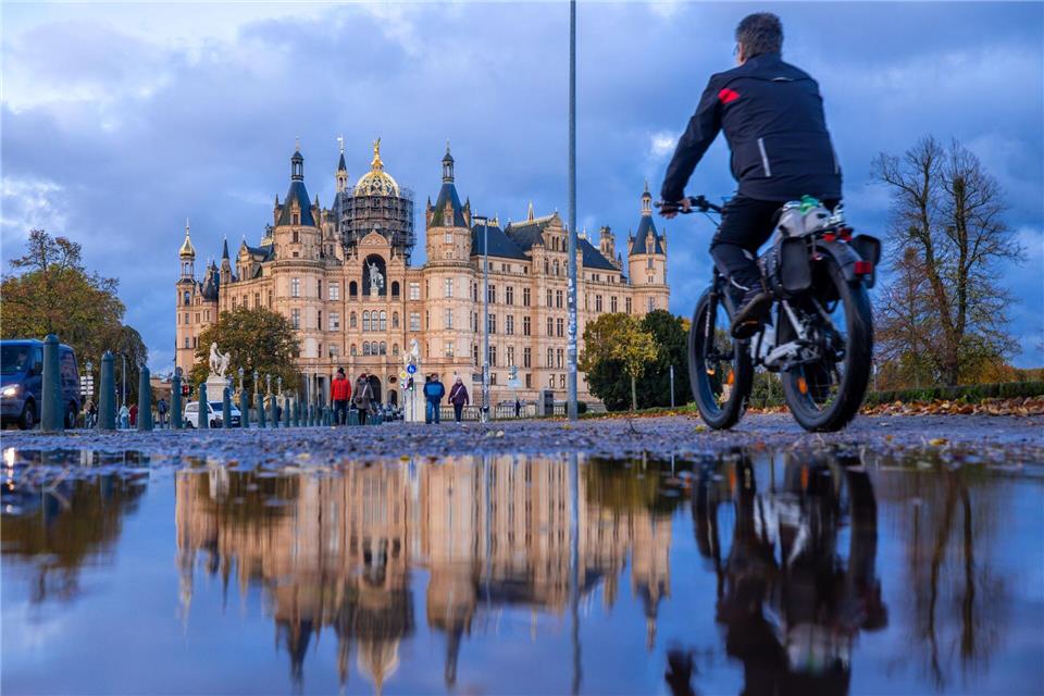 Bilder des Tages  Herbstwetter in Norddeutschland: Ein Radfahrer fährt an einer Pfütze vorbei, in der sich das Schweriner Schloss spiegelt.Jens Büttner/dpa