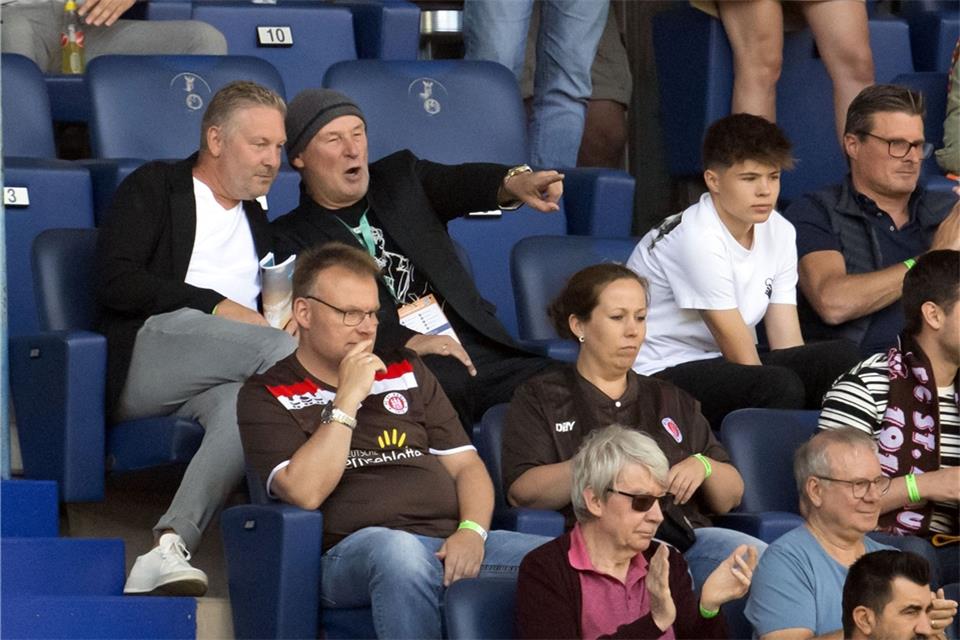 Hermann Tecklenburg sitzt auf der Tribüne und zeigt aufs Spielfeld.