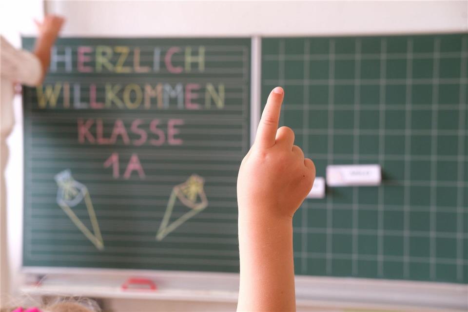 „Herzlich willkommen Klasse1 A“ steht an der Tafel eines Klassenzimmers, während sich ein Kind meldet. Am Samstag wird in Sachsen Einschulung gefeiert.Sebastian Willnow/dpa
