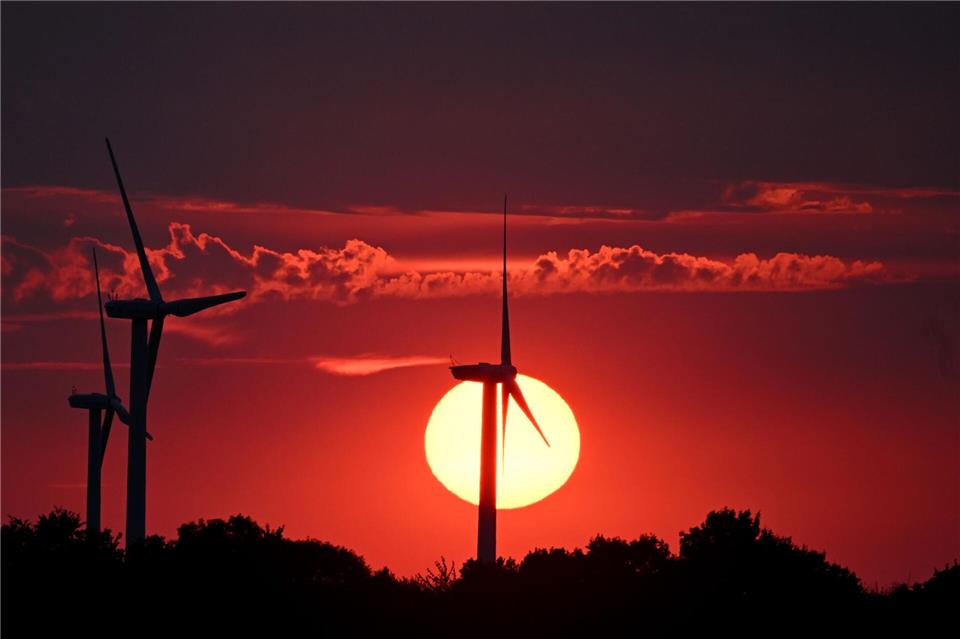 Hinter Windrädern färbt die sinkende Sonne den Himmel über Nordrhein-Westfalen rot. Federico Gambarini/dpa