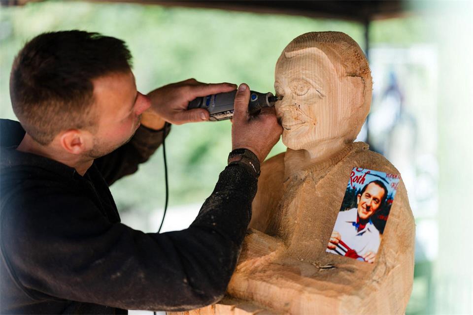 Holzschnitzkünstler Marcel Lesser hat ein Foto von Herbert Roth dabei. Mit den Figuren soll dem Volksmusiker ein Denkmal gesetzt werden.Michael Reichel/dpa