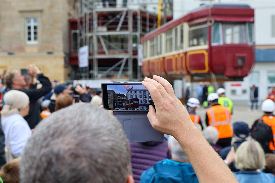 Hunderte Schaulustige verfolgen die Platzierung des Schwebebahnwagens auf einer Stahlkonstruktion zwischen zwei Gebäude. Matthias Rosenkranz/dpa