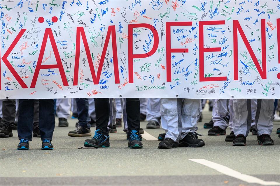 In ihren Overalls stehen Beschäftige des Motorenwerks von Volkswagen in Chemnitz hinter einem Banner mit der Aufschrift „KÄMPFEN!“.Hendrik Schmidt/dpa