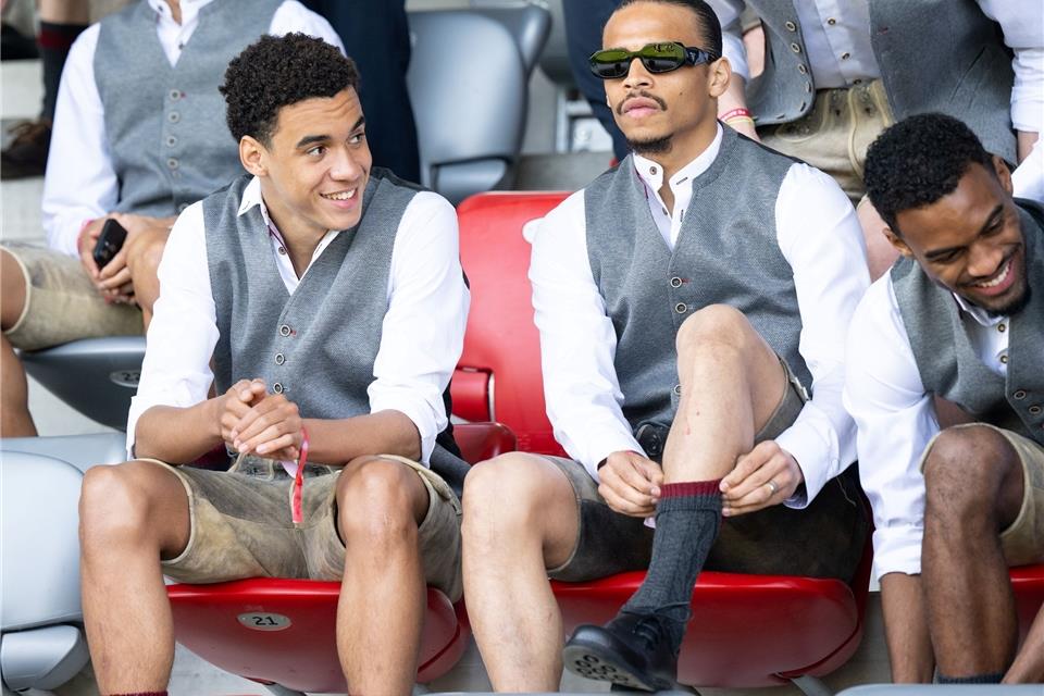 Jamal Musiala (l) und Leroy Sane von München verfolgen das Spiel der Frauen in Tracht auf der Tribüne.