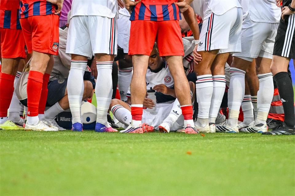 Jamal Musiala sitzt, abgeschirmt von Münchner Teamkollegen und Heidenheimer Fußballern, nach seinem Zusammenbruch auf dem Rasen. Harry Langer/DeFodi/dpa/dpa