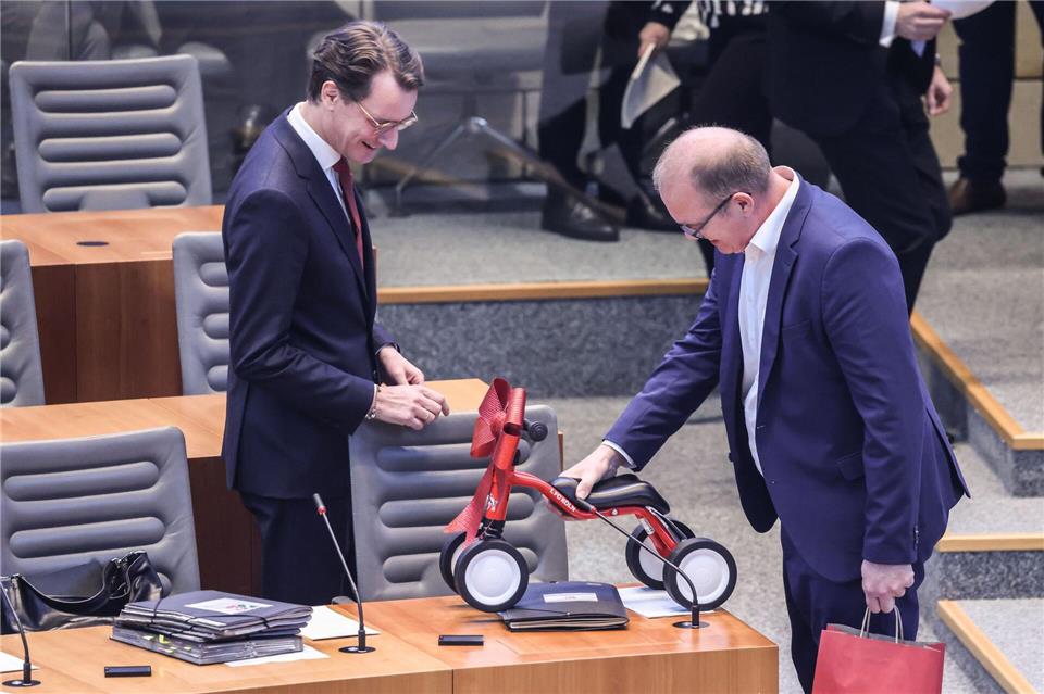 Jochen Ott (SPD, r.) überreicht Hendrik Wüst (CDU) das 1. FC-Köln-Laufrad im Plenarsaal des Landtags.Oliver Berg/dpa