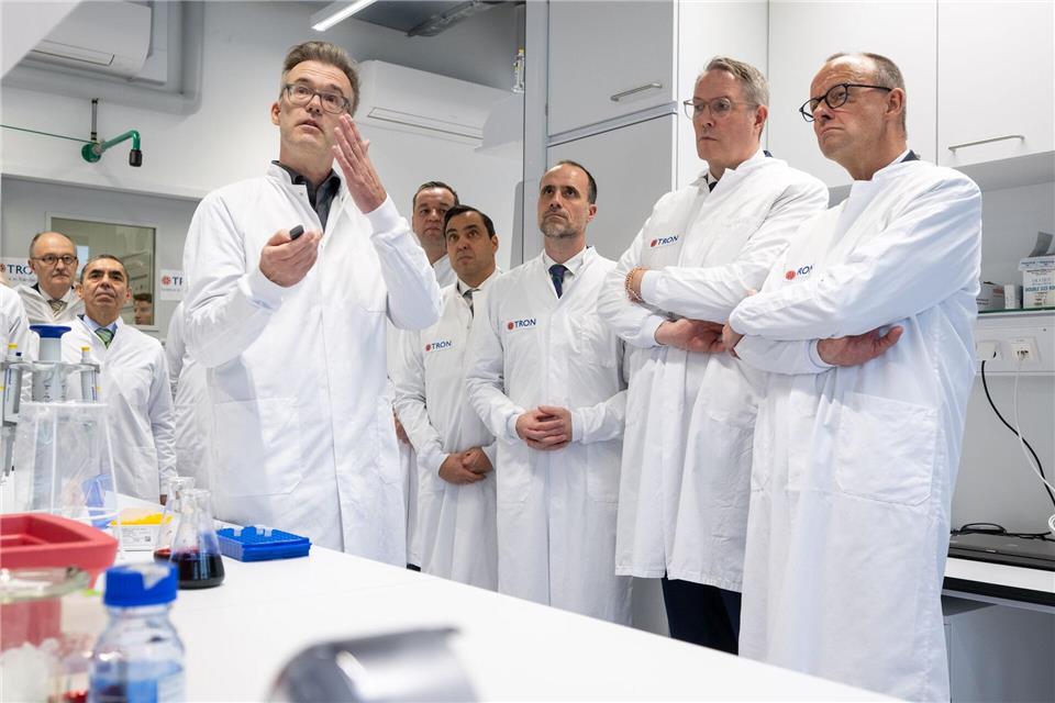 Kanzler Merz, Ministerpräsident Schweitzer und der rheinland-pfälzische Wissenschaftsminister Hoch bekommen ein Projekt erklärt, bei dem Hefe für die Produktion von RNA genutzt werden soll. Harald Tittel/dpa