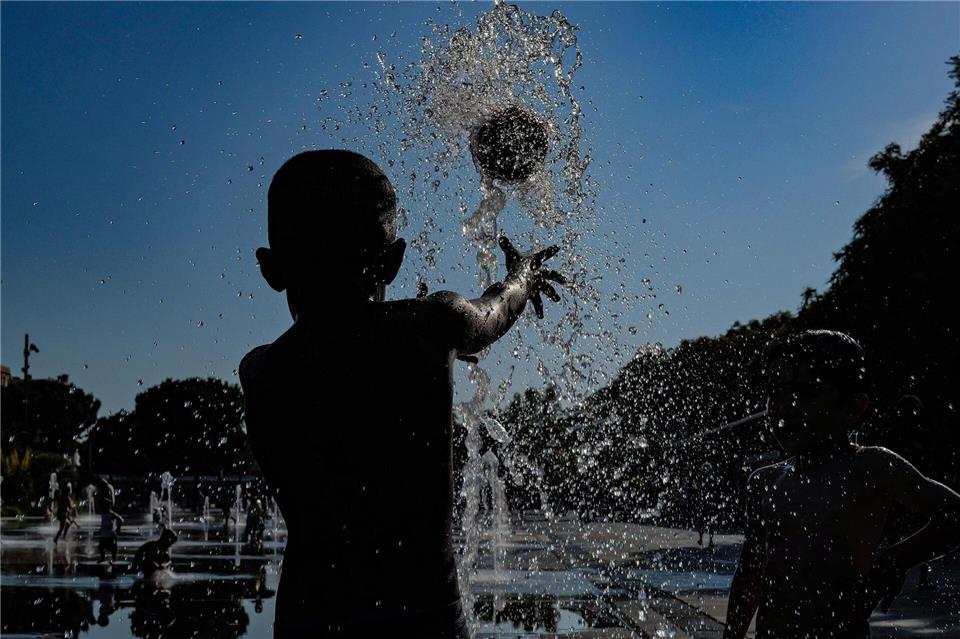 Kinder spielen mit einem Ball in einem Springbrunnen in Nizza.Valery Hache/AFP/dpa