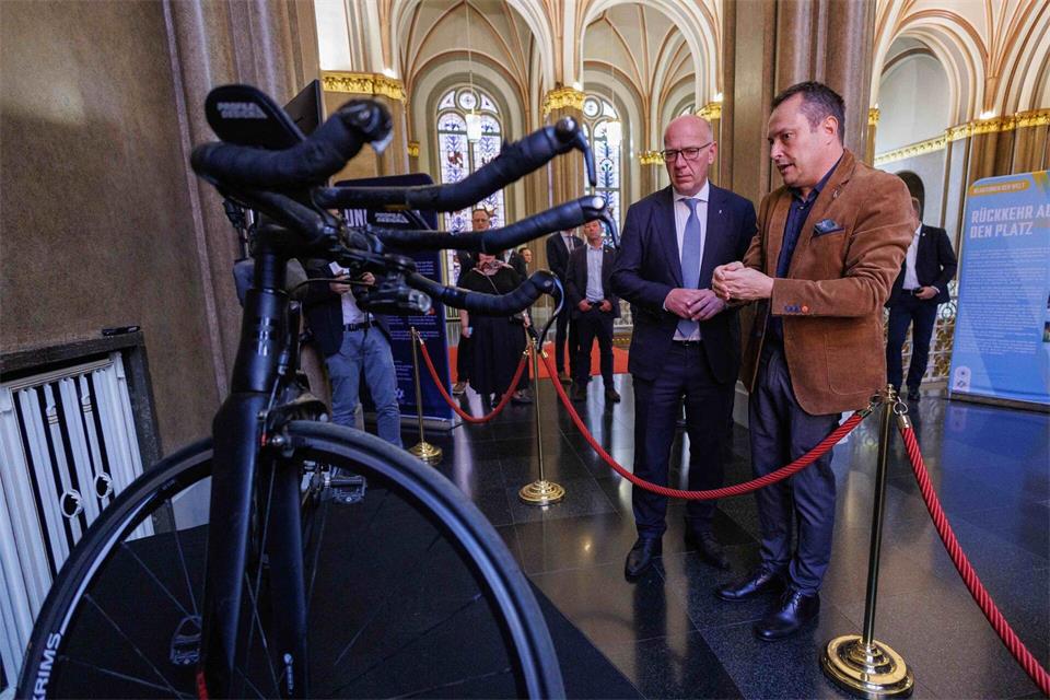 Kurator Adi Rubinstein (r.) zeigt Berlins Regierendem Bürgermeister Kai Wegner (CDU) das Fahrrad von Lior Waitzman.Carsten Koall/dpa
