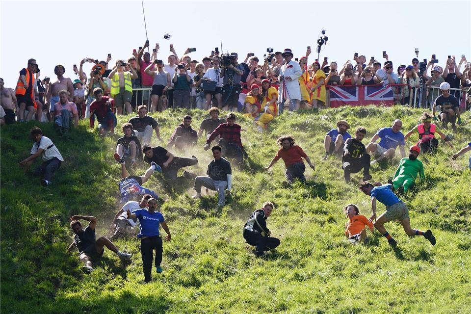 Kurioser Kultlauf in Gloucestershire: Beim Käserennen 2026 rennen Männer dem rollenden Käselaib den Hügel hinunter nach.Jacob King/PA Wire/dpa