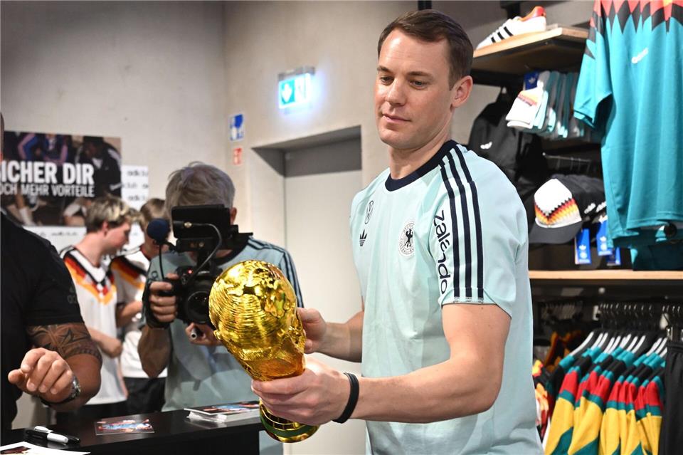 Lächelnd signiert Manuel Neuer einen goldenen WM-Pokal. Federico Gambarini/dpa