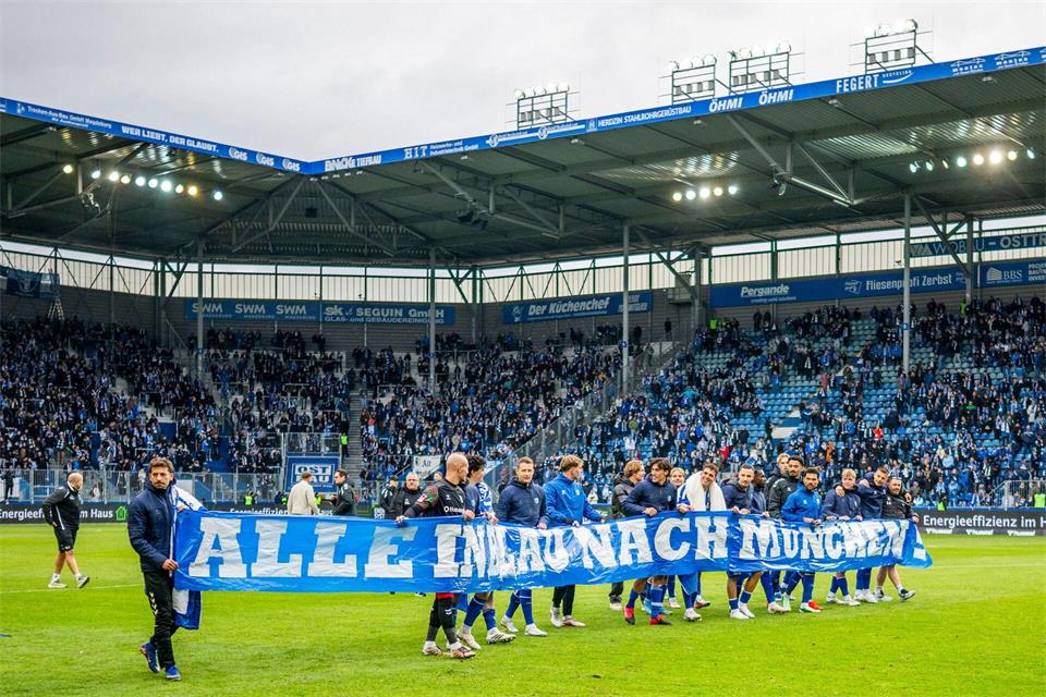 Magdeburgs Spieler tragen nach dem Spiel gegen den KSC ein Banner mit der Aufforderung „Alle in Blau nach München“Julius Frick/dpa