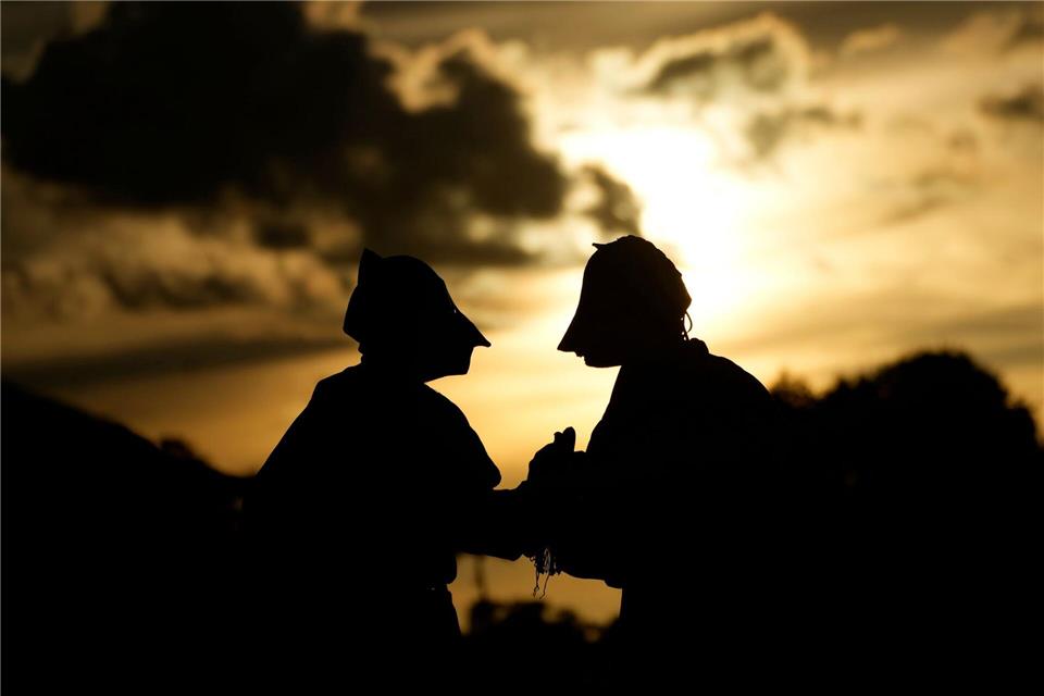 Maskierte Freischärler schauen sich bei Sonnenuntergang eine traditionelle Reitershow an.Eraldo Peres/AP/dpa