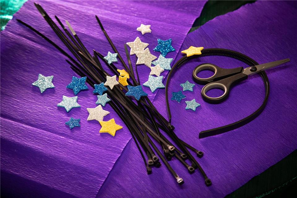 Material für den Sternen-Kopfschmuck: schwarze Kabelbinder, ein Haarreif, selbstklebende Glitzersterne aus Moosgummi und eine Schere.Christin Klose/dpa-tmn
