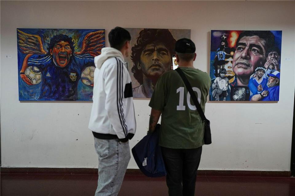 Menschen betrachten eine Kunstausstellung mit Bildern des verstorbenen Fußballstars Maradona.Natacha Pisarenko/AP/dpa