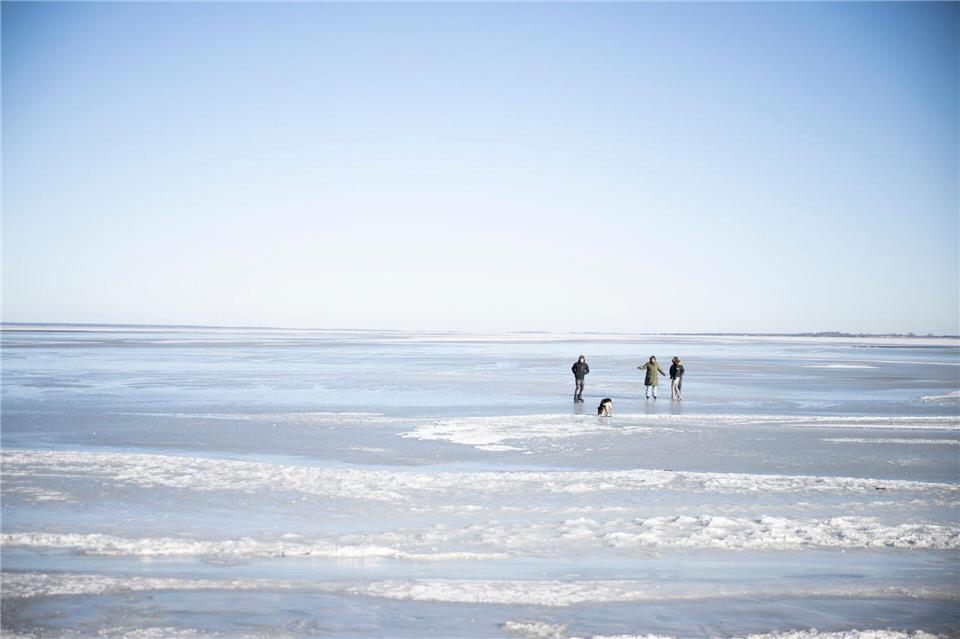 Menschen erkunden an der Küste die vergänglichen Eiswelten. Philip Dulian/dpa