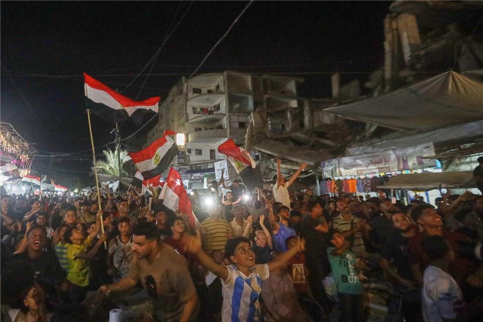 Menschen schwenke agyptische Flaggen und verfolgen im zentralen Gazastreifen das WM-Spiel Ägypten gegen Belgien auf einer Großbildleinwand.Yousef Al Zanoun/AP/dpa