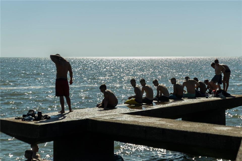 Menschen sitzen auf einem Dock in Montevideo.Matilde Campodonico/AP/dpa