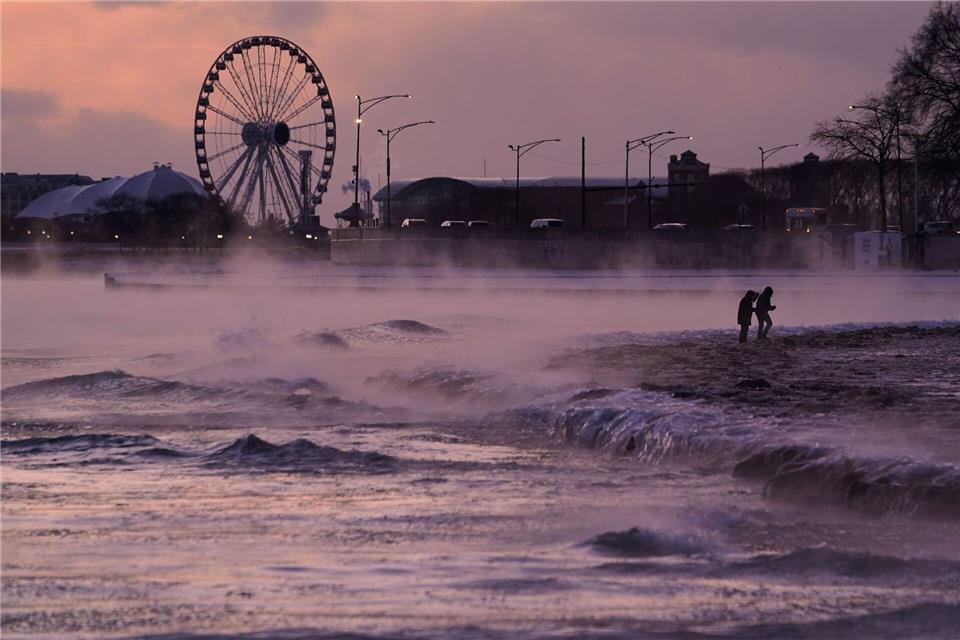 Menschen spazieren in Chicago über einen mit Eis bedeckten Strand am Ufer des Michigansees.Kiichiro Sato/AP/dpa